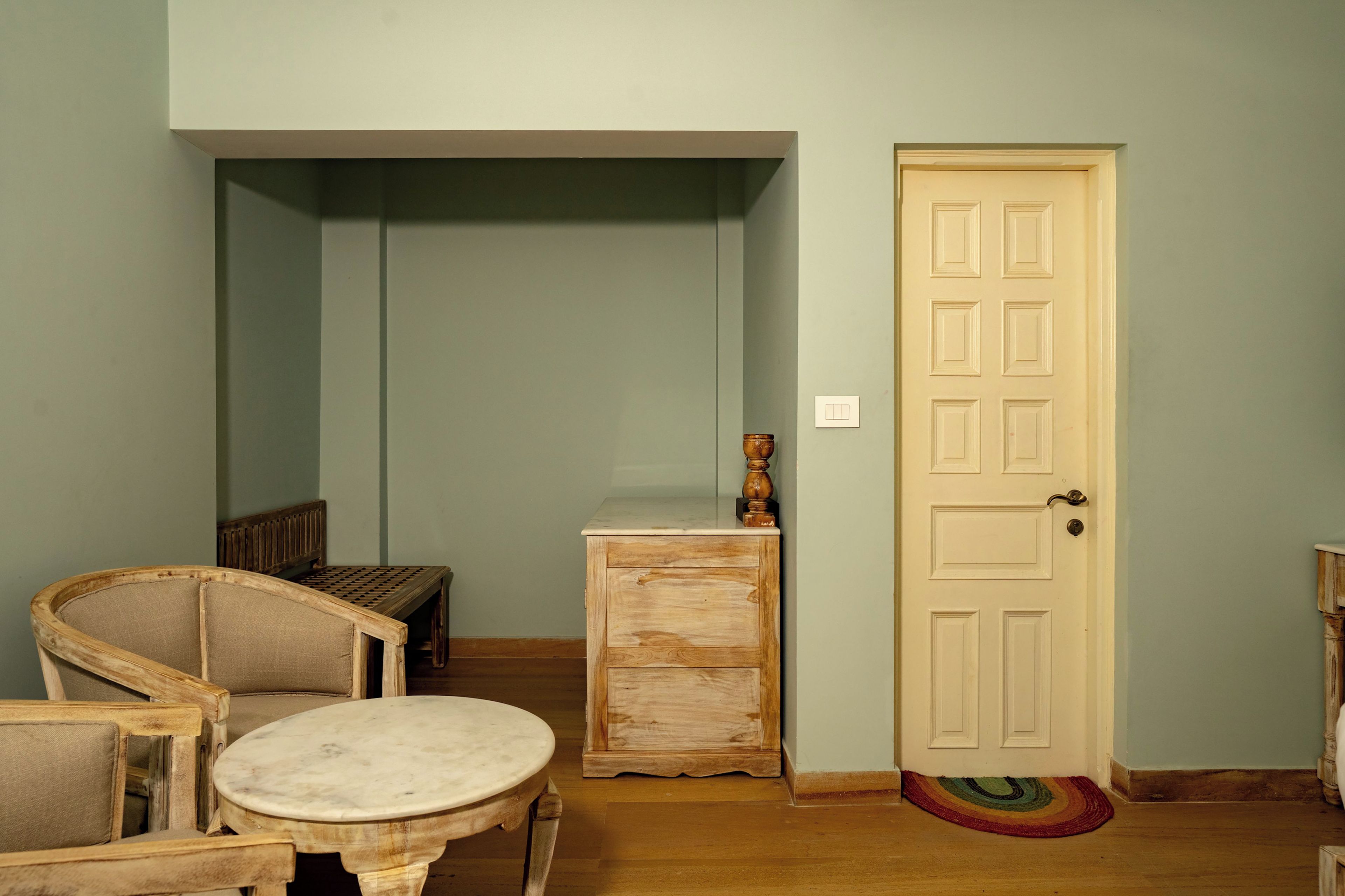 Una habitación con un banco de madera, una mesita y una puerta con felpudo.