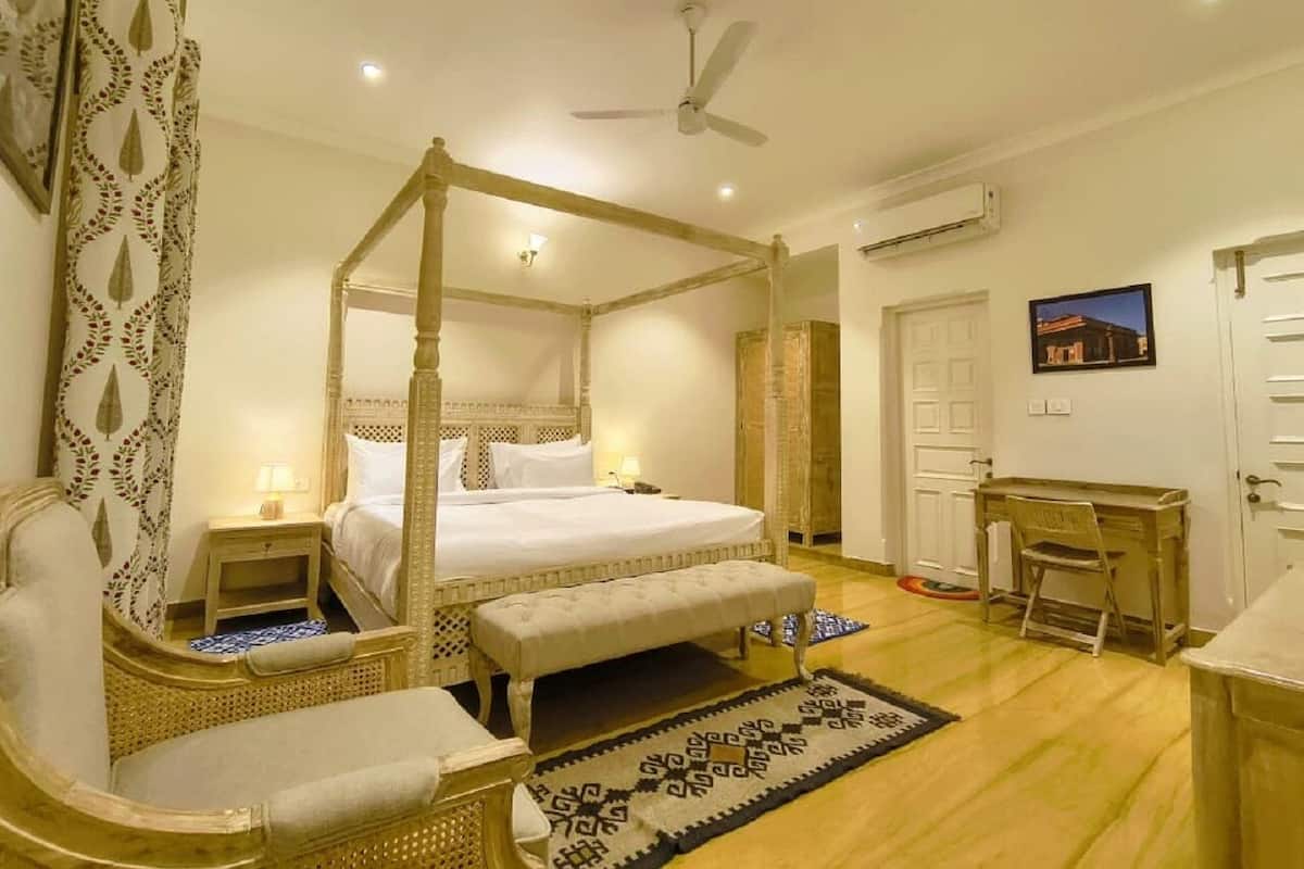 Una cama con dosel y cuatro columnas, un escritorio de madera, una silla y una mesita de noche con lámpara.