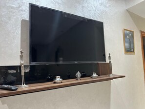 A flat-screen TV mounted on a wall above a wooden shelf with decorative items. - Apartment rte immouzer (Fès)