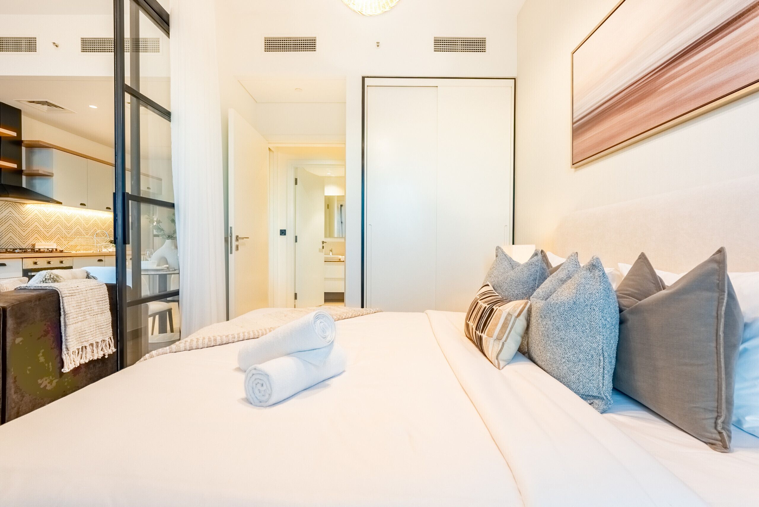 A hotel room with a neatly made bed, a large mirror, and a view of the hallway.