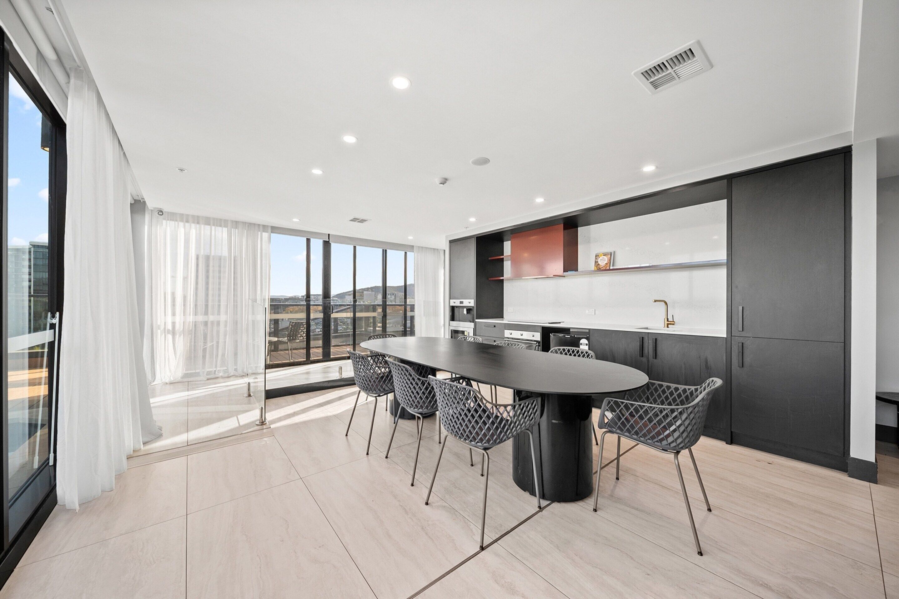 A modern kitchen with a large island, black cabinets, and a view of the city.