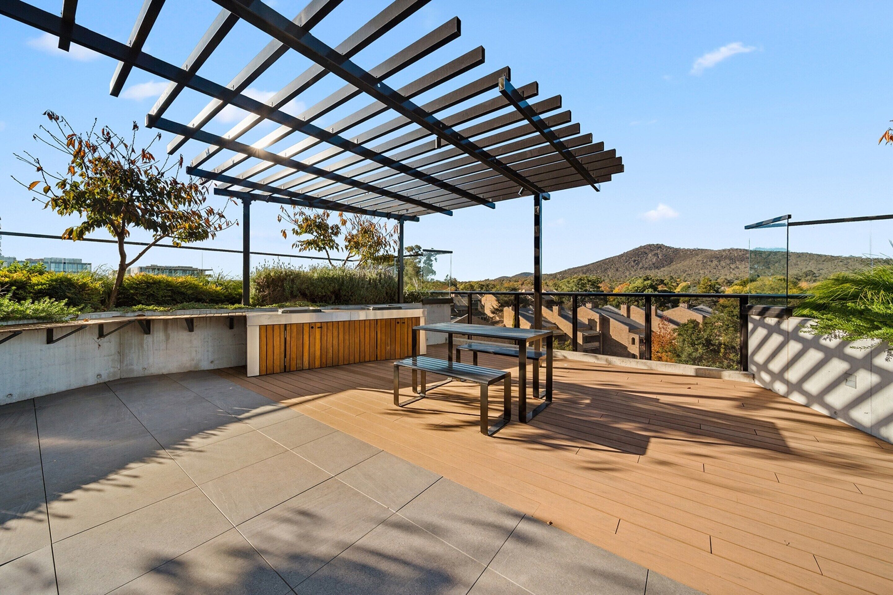 Een terras buiten met een pergola, een zithoek en uitzicht op een glooiend landschap.
