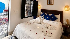 A hotel room with a bed, a chandelier, a window with metal bars, a picture on the wall, and a door leading outside. - Riad lazord de Marrakech  (Marrakech)