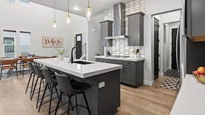 Una cocina moderna con una isla central, taburetes de bar, luces colgantes y un salpicadero con diseño geométrico.