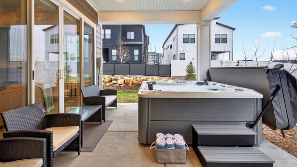 Un patio moderno al aire libre con jacuzzi, mobiliario de mimbre y vistas de edificios cercanos.