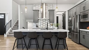 Una cocina moderna con una isla grande, taburetes de bar, electrodomésticos de acero inoxidable y un salpicadero con diseño.
