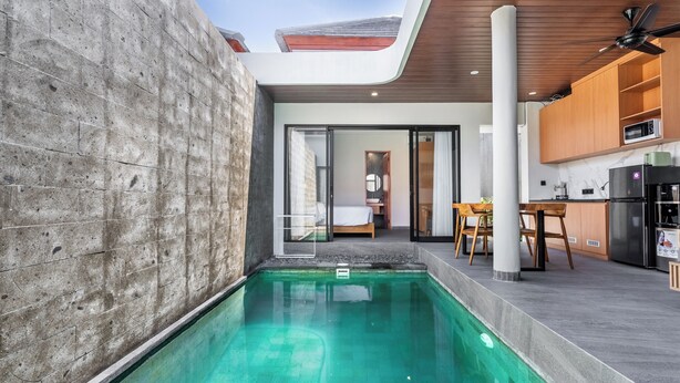 Un área de piscina moderna con un muro de concreto, techo de madera y cocina con gabinetes y electrodomésticos de madera.