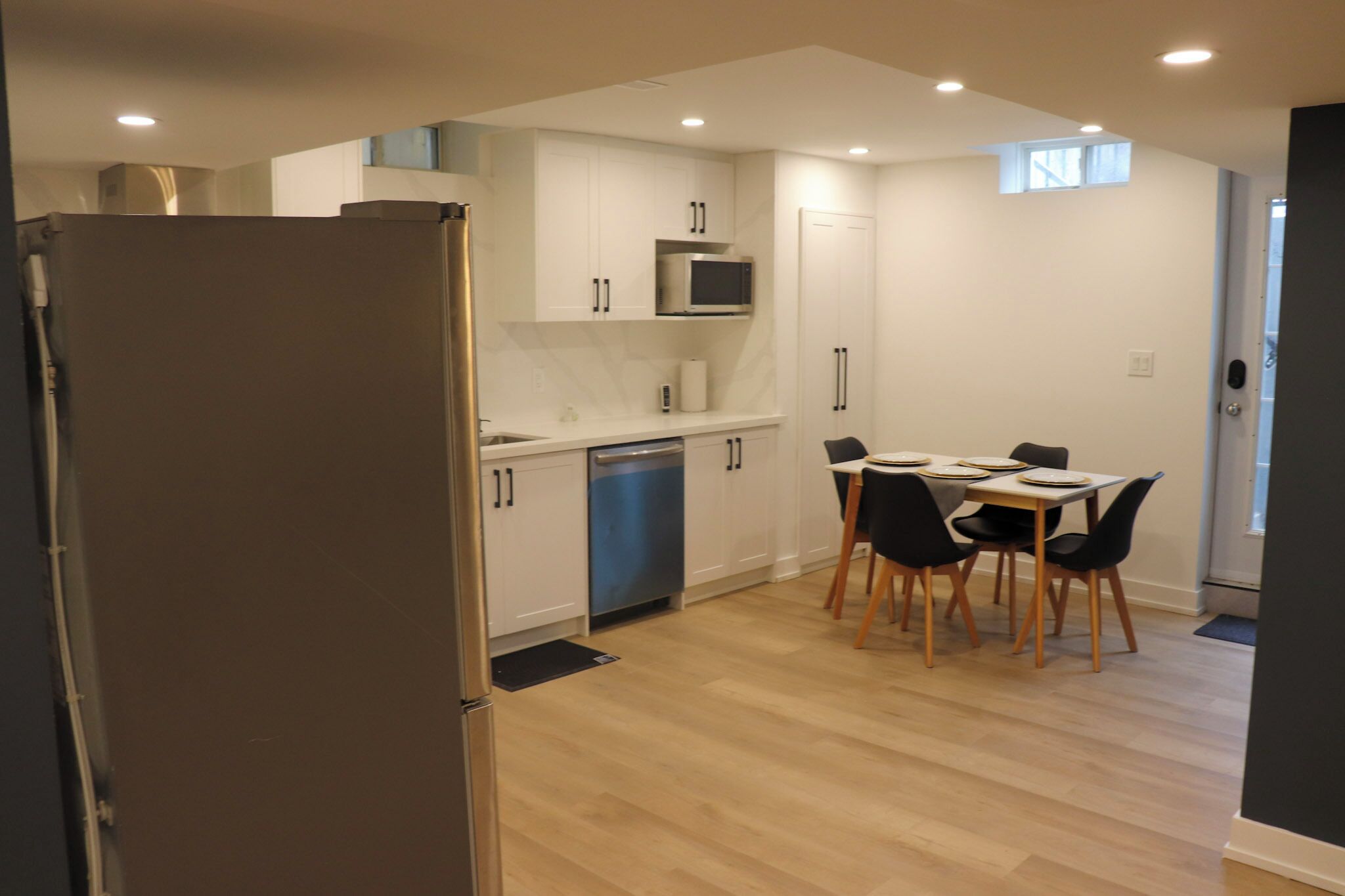 A modern kitchen with white cabinets, a stainless steel refrigerator, a microwave, and a dining area with a table and chairs.