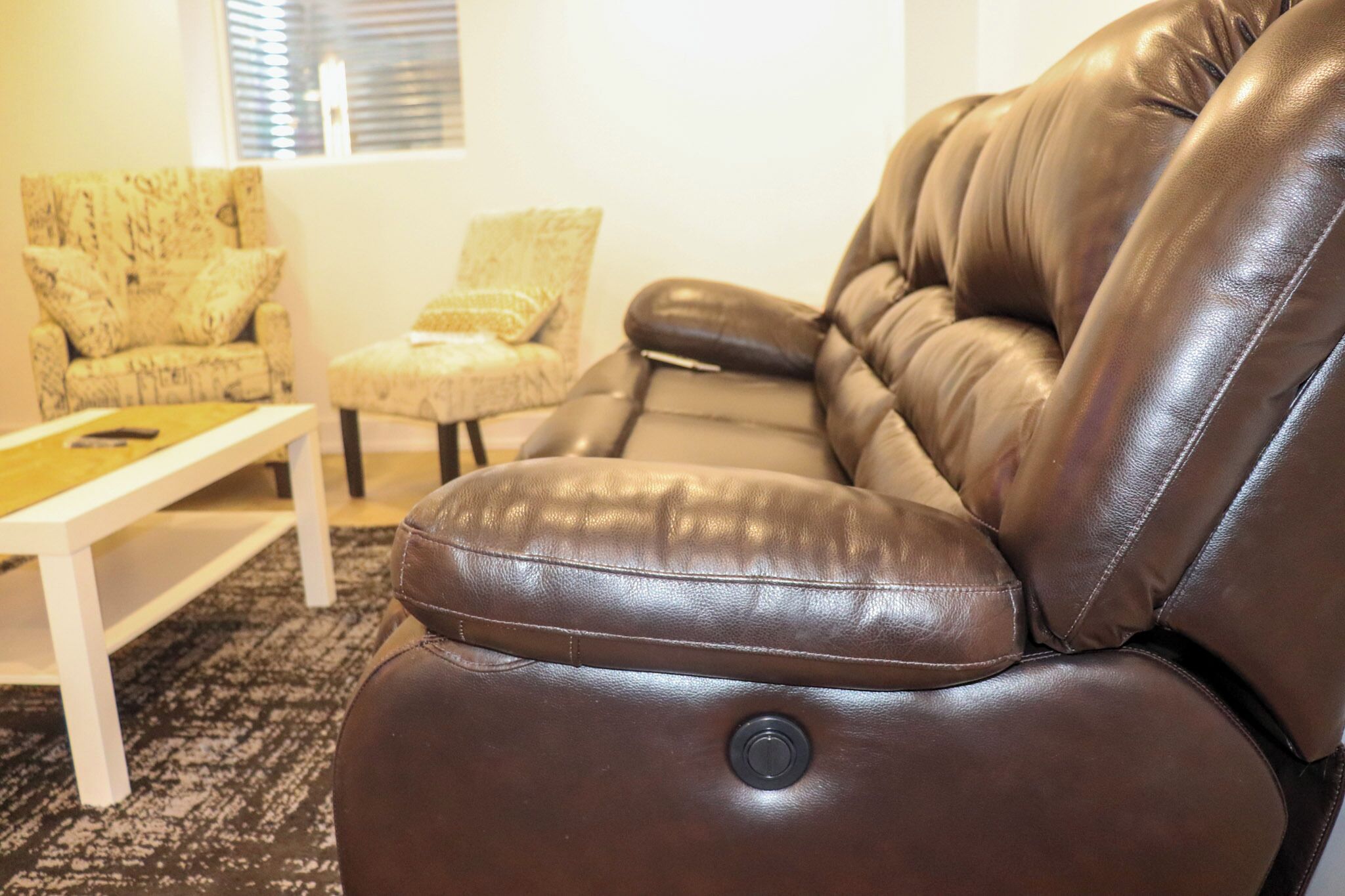 A brown leather sofa with a button, a patterned armchair, and a small table in a living room.