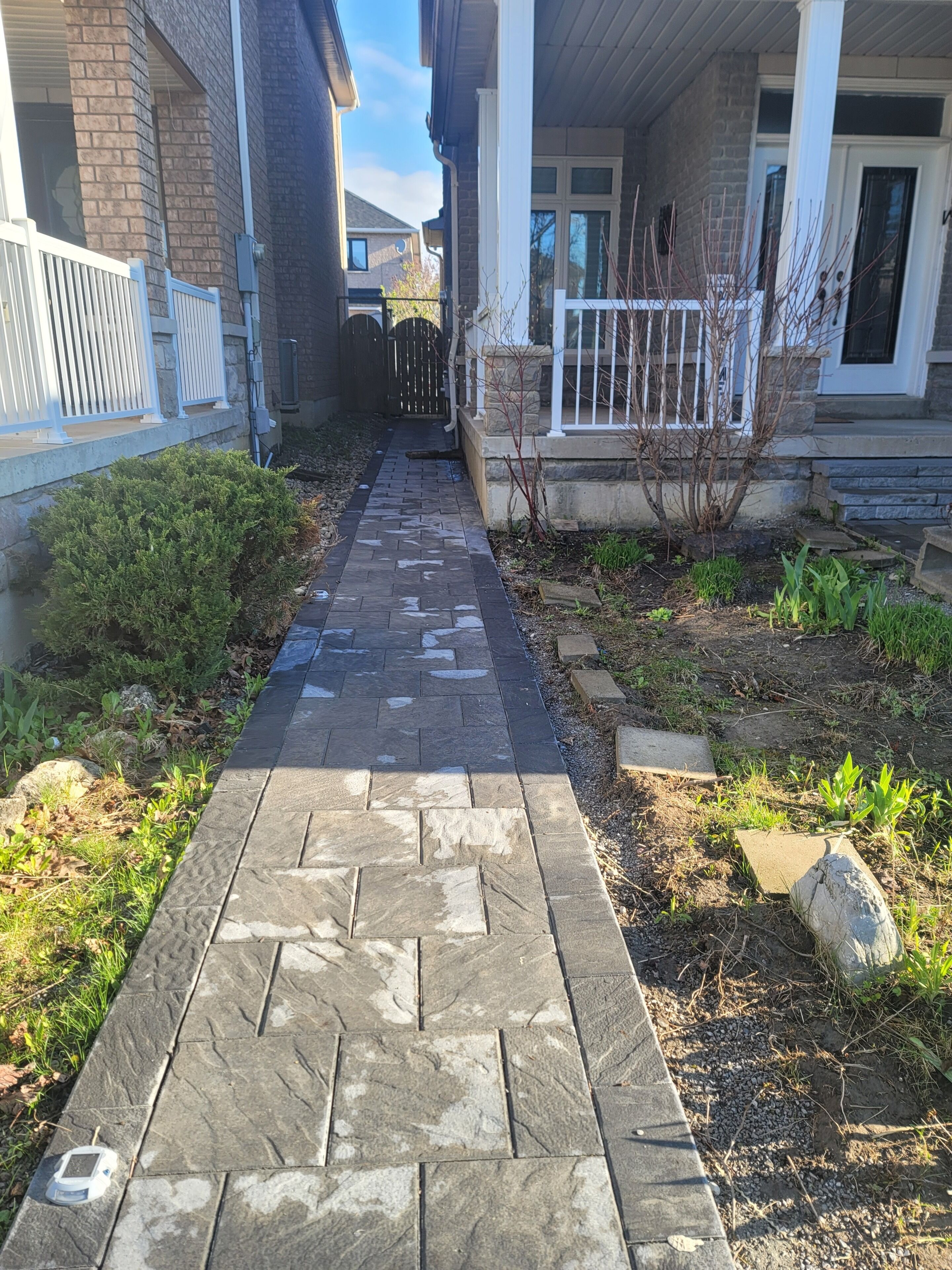 Un chemin pavé mène à une maison dont la façade est en pierre, ornée d’une balustrade blanche et bordée d’un petit jardin.