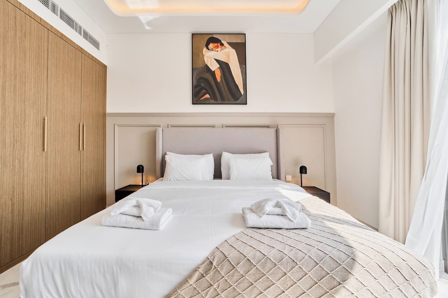 A hotel room with a large bed, two bedside tables, a wardrobe, and a painting on the wall.