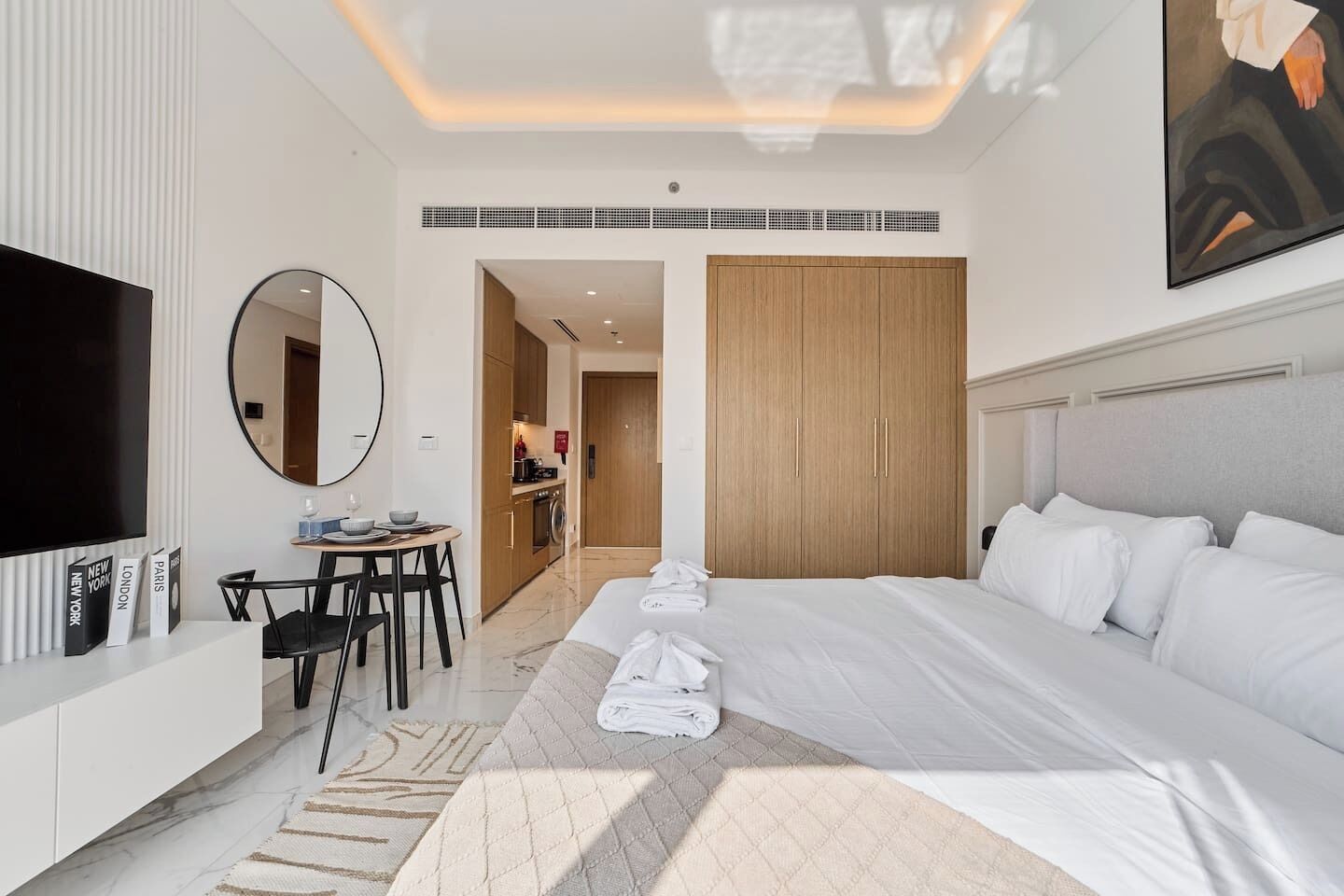 A modern hotel room with a large bed, a TV, a dining area, and a walk-in closet.