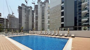 A swimming pool with lounge chairs and a view of high-rise buildings. - Elegant Studio in Azizi Riviera | Perfect Getaway (Dubai)