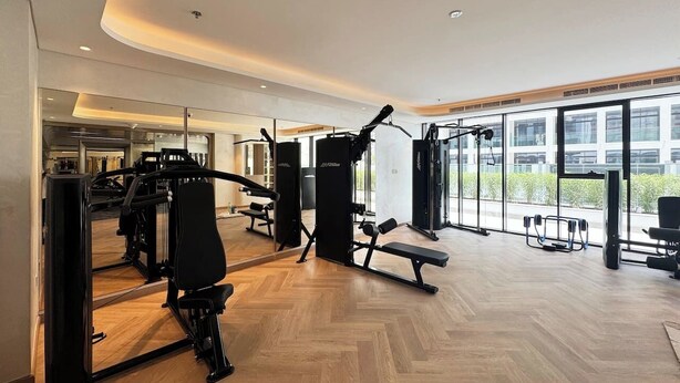 A modern gym with various exercise machines, a wooden floor, and large windows offering natural light. - Elegant Studio in Azizi Riviera | Perfect Getaway (Dubai)
