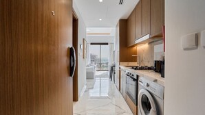 A modern kitchen with wooden cabinets, a built-in oven, and a washing machine. - Elegant Studio in Azizi Riviera | Perfect Getaway (Dubai)