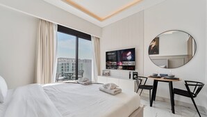 A hotel room with a large bed, a desk with two chairs, a TV mounted on the wall, and a large mirror. - Elegant Studio in Azizi Riviera | Perfect Getaway (Dubai)