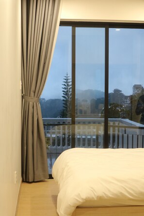 A bedroom with a large window, a bed, and a view of a balcony and buildings. - Famille Hotel Da Lat (Xuan Huong - Da Lat)