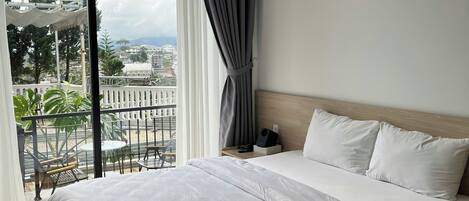 A modern hotel room with a large bed, a balcony with outdoor furniture, and a view of the cityscape.
