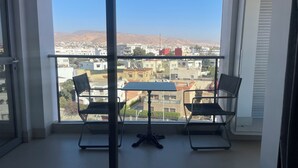 A balcony with a table and chairs, offering a view of a cityscape with buildings and mountains in the distance. - Beautiful apartment in downtown Agadir at Galerie Talborjt (Agadir)
