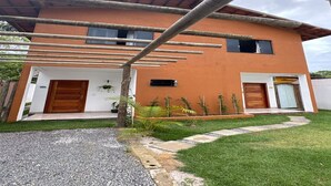 A two-story house with a modern design, featuring a wooden pergola over the entrance, a gravel driveway, and a well-maintained lawn. - Village House in the Valley (Arraial d'Ajuda)