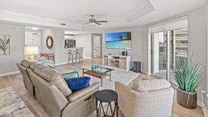 A modern living room with a sofa, coffee table, and a TV displaying a beach scene. - Royale Palms 804 2 Br Oceanview in Kingston, Pool (Myrtle Beach)