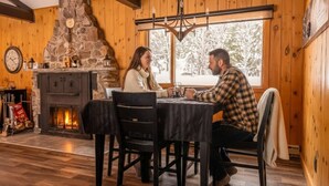 Une pièce chaleureuse avec une cheminée en pierre, des murs en bois et une table à manger entourée de chaises.