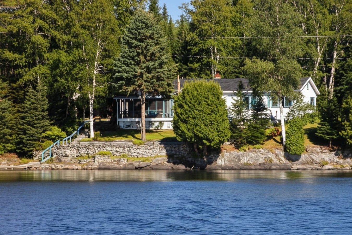 A lakeside property with a house, a covered deck, and a stone staircase leading to a dock.