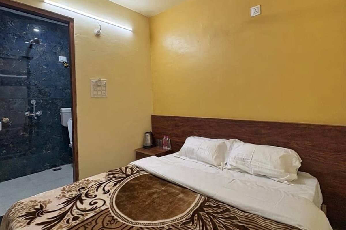 Una habitación de hotel con cama, cabecera de madera, mesita de noche y baño visible a través de una puerta abierta.