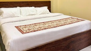Een net opgemaakt bed met witte lakens en een decoratieve plaid, een houten hoofdbord en een aan de muur hangend schilderij van een landschap.