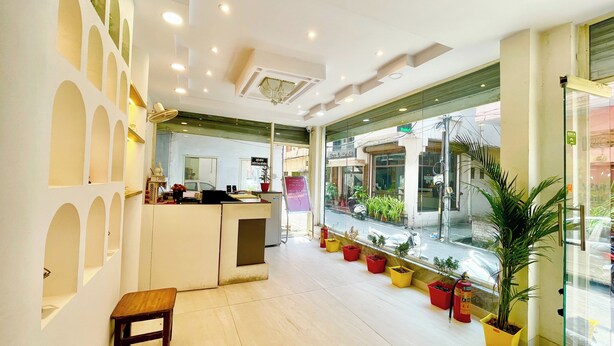 A hotel reception area with a check-in counter, a small seating area, and a view of the street through large windows. - HOTEL PREMIUM K P  Near HAR KI PODDI   (Haridwar)