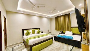 A hotel room with a bed, a desk, a chair, a television, and a ceiling fan. - HOTEL PREMIUM K P  Near HAR KI PODDI   (Haridwar)