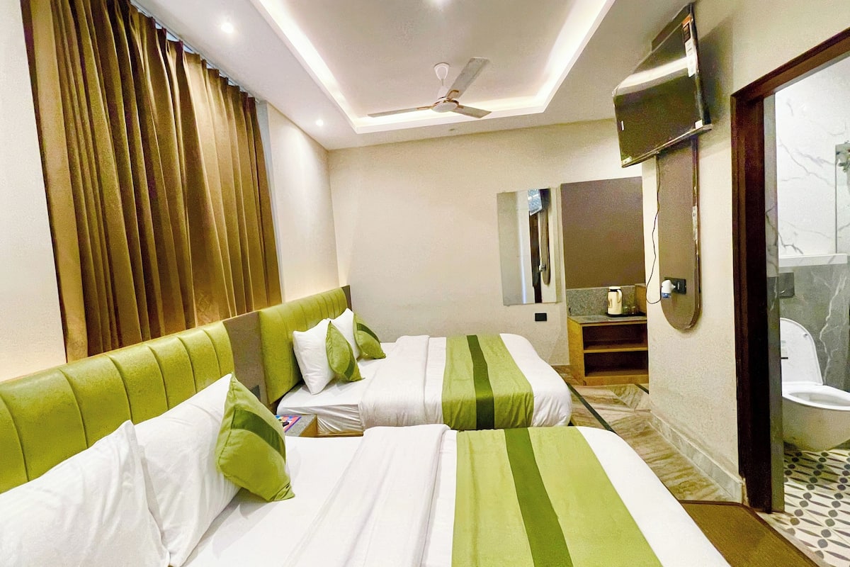 Une chambre d’hôtel avec deux lits, un ventilateur de plafond, une salle de bain avec des toilettes et un lavabo, et un miroir.