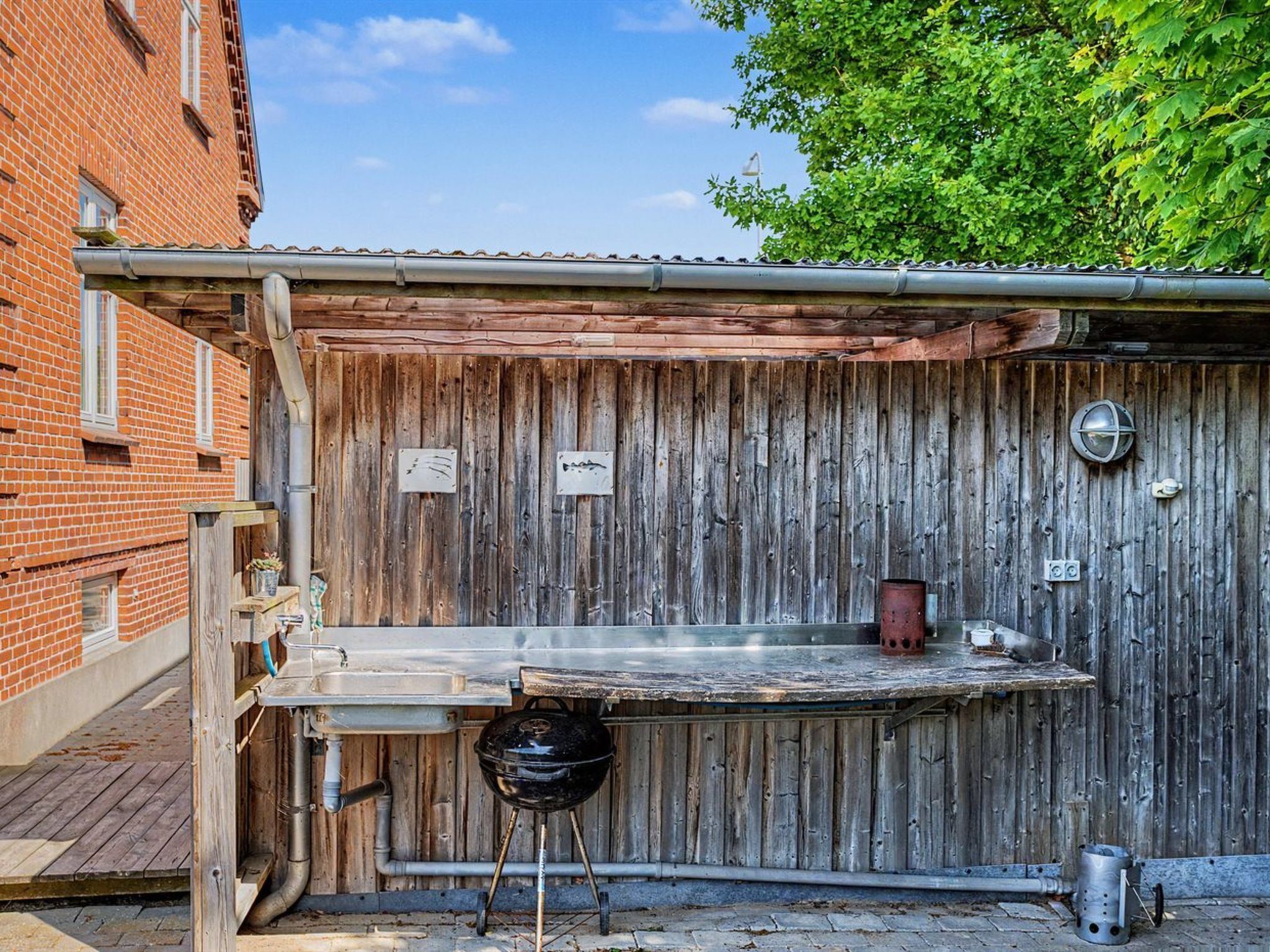 Un espace barbecue extérieur de style rustique, avec une clôture en bois, un gril en métal et une poubelle.