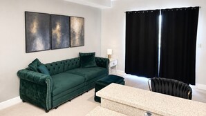 A living room with a green sofa, a coffee table, a black chair, a ceiling fan, and a window with black curtains. - Walk to FSU, Downtown & the Capitol-PRIME location (Tallahassee)