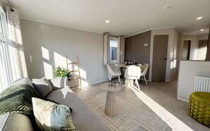 A living room with a sofa, a small round table, and a dining area with chairs. - Comfortable Family Chalet in Hollum (Hollum)