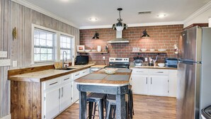 Una cocina con isla de madera, armarios blancos, salpicadero de ladrillo y electrodomésticos de acero inoxidable.