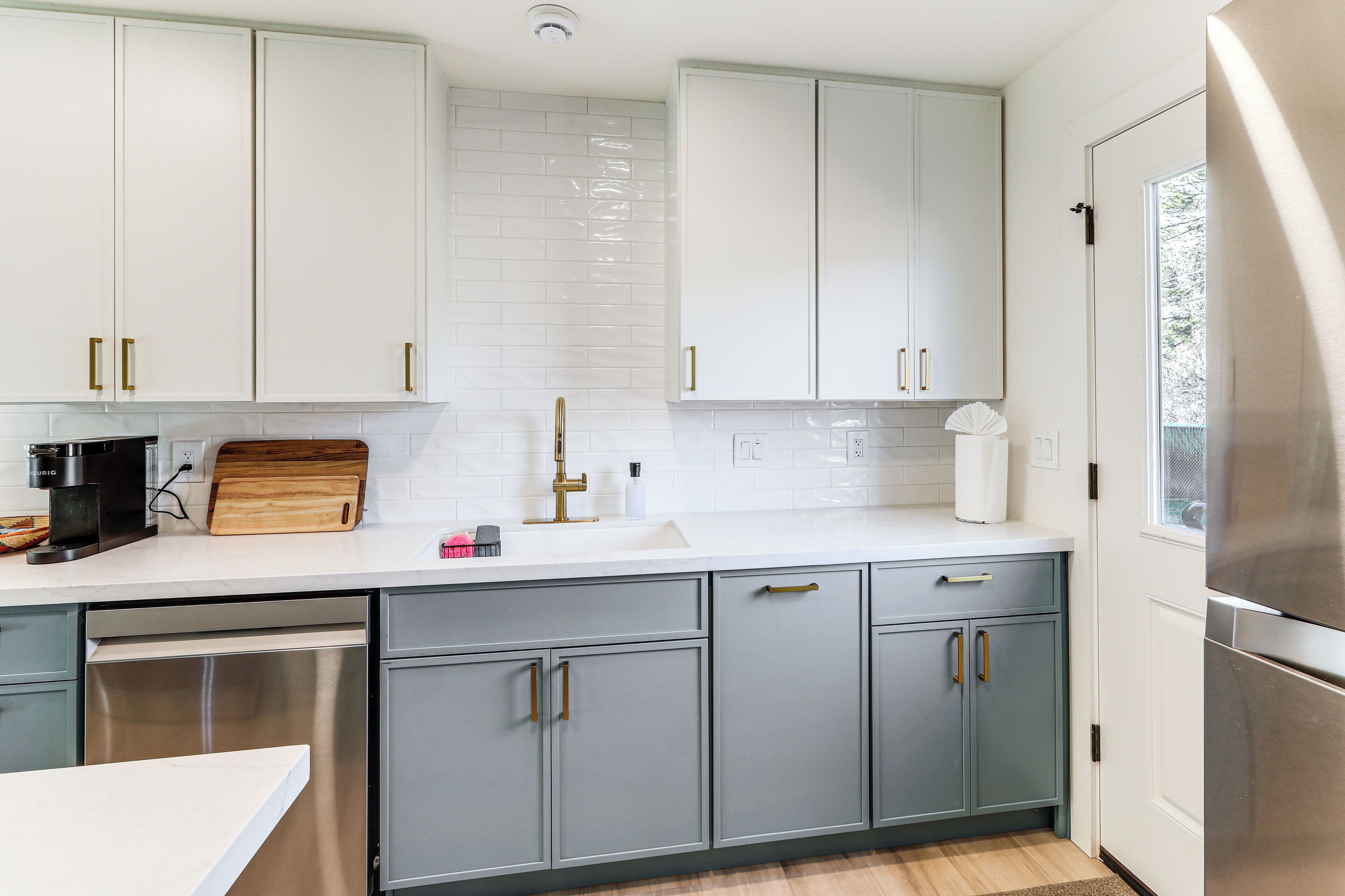 Une cuisine moderne avec des meubles gris, des plans de travail blancs et des appareils électroménagers en acier inoxydable.