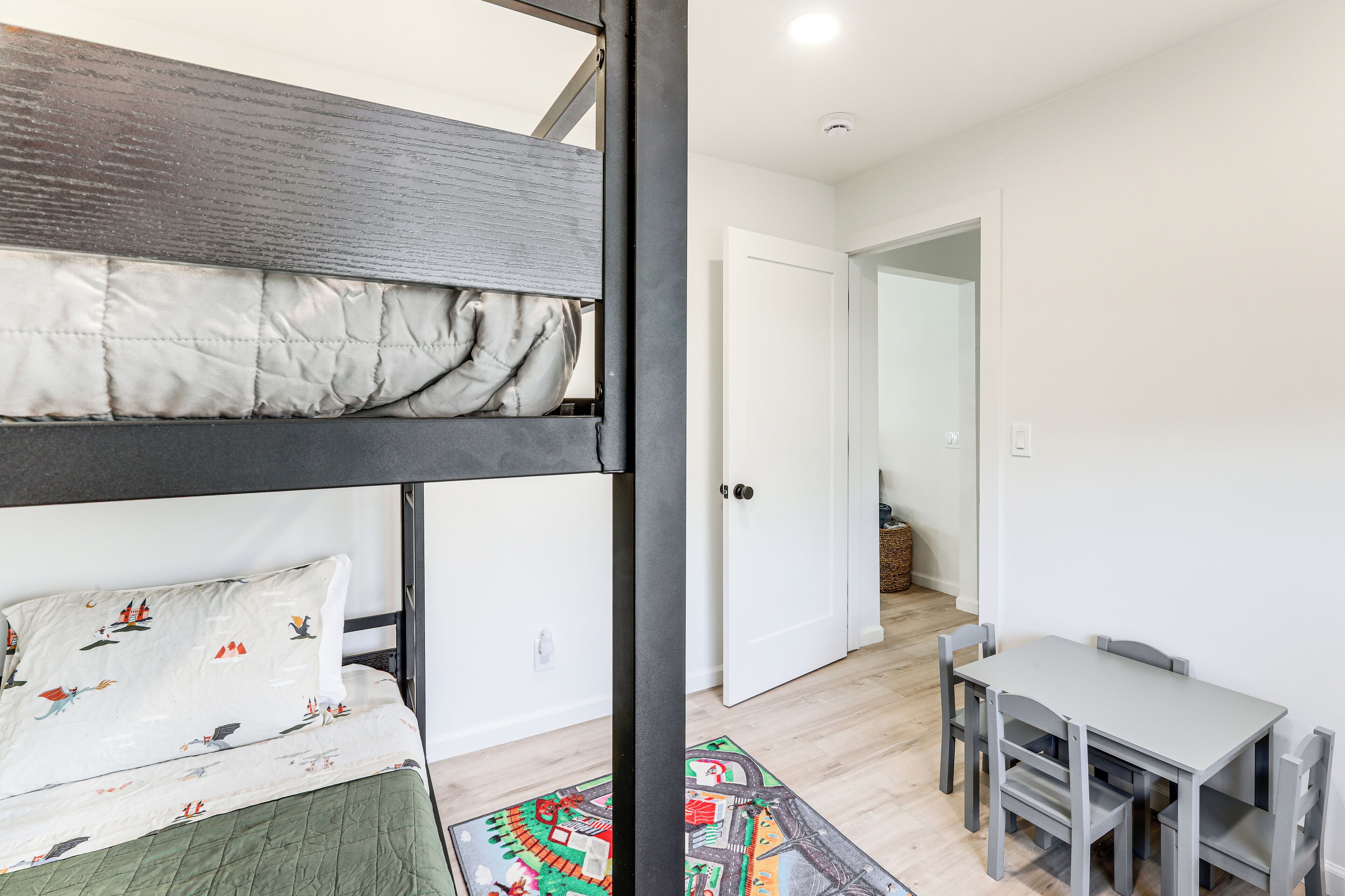 A bunk bed with a quilted mattress, a small table with chairs, and a colorful rug.
