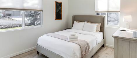 A bedroom with a bed, a nightstand, a lamp, and a window with blinds.