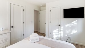 Une chambre à coucher moderne, avec un lit, un téléviseur fixé au mur et une porte donnant sur une autre pièce.