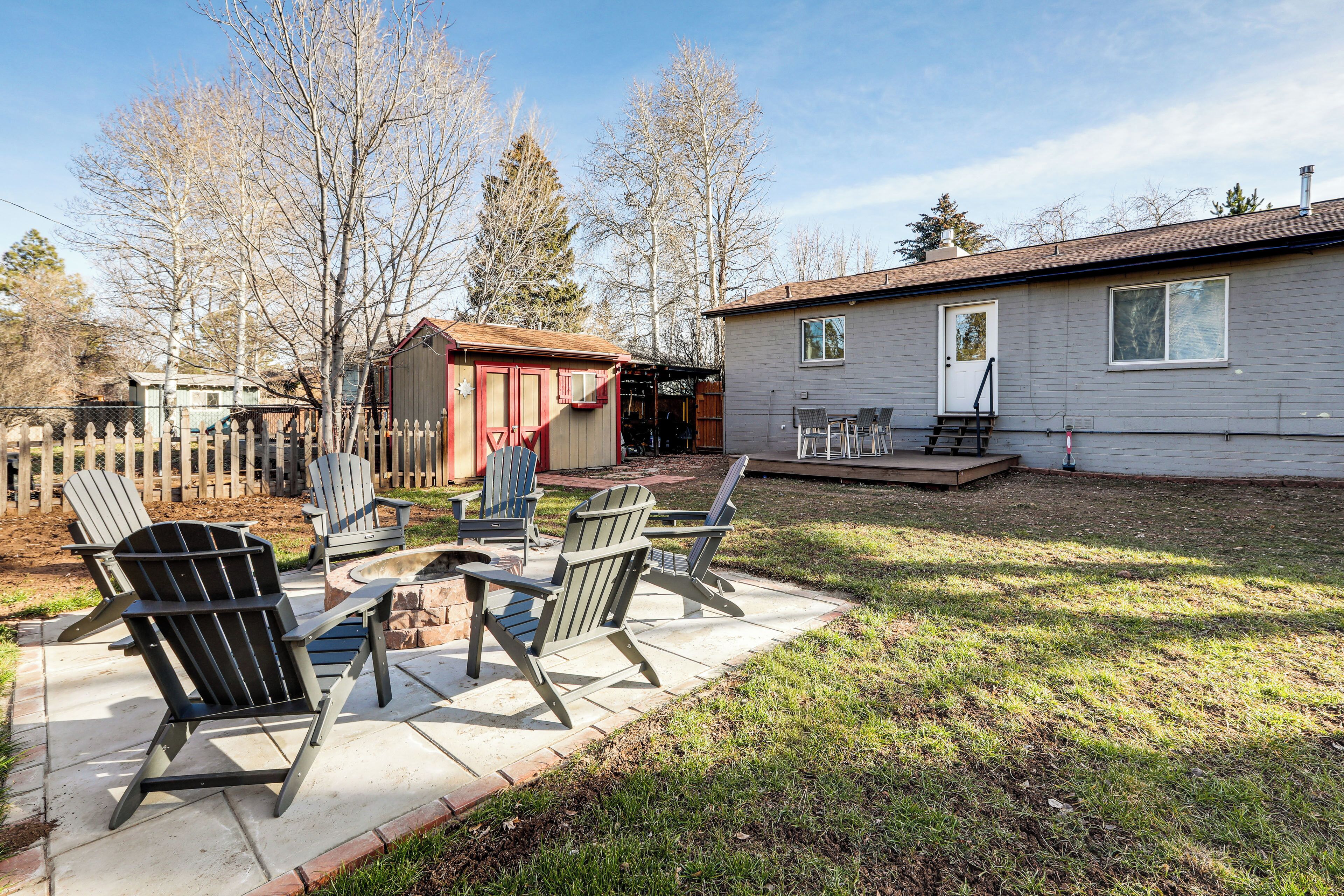 Ein Garten mit Terrasse, Adirondack-Stühlen, einem kleinen Schuppen und einem Haus.