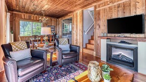 A wooden interior with a fireplace, leather chairs, and a TV. - 2BR Oceanfront Cottage w/ Fire Table & Huge Deck (Point Roberts)