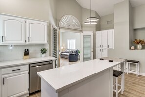 A modern kitchen with white cabinetry, a central island, and a dishwasher. - Stunning Renovated 5BR House W/pool 7 mil to Strip (Las Vegas)