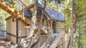 Une maison en bois à plusieurs étages, avec un escalier menant aux niveaux supérieurs, entourée d’arbres.