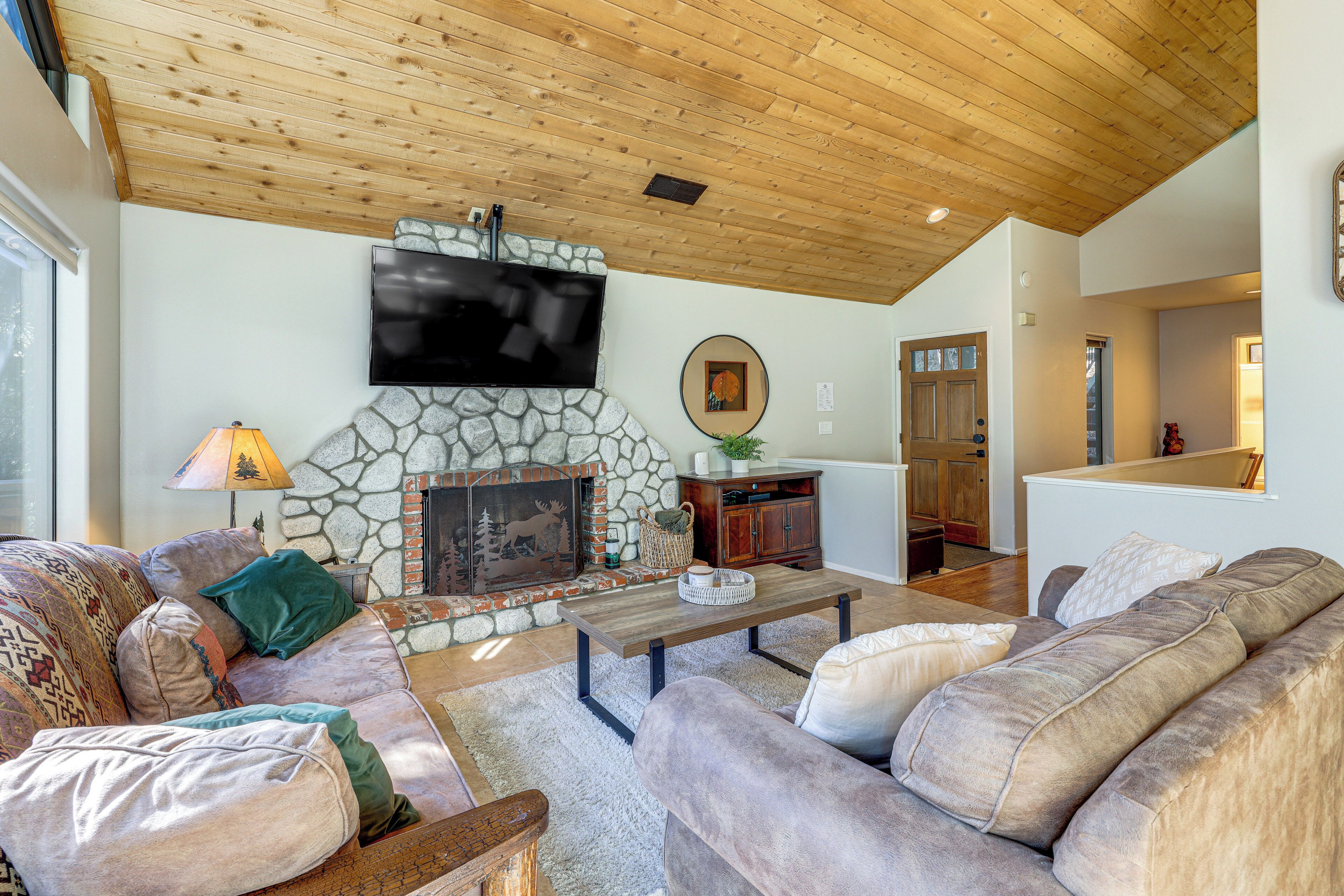 A cozy living room with a stone fireplace, wooden ceiling, and a flat-screen TV mounted above it.