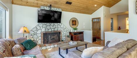 A cozy living room with a stone fireplace, wooden ceiling, and a flat-screen TV mounted above it.