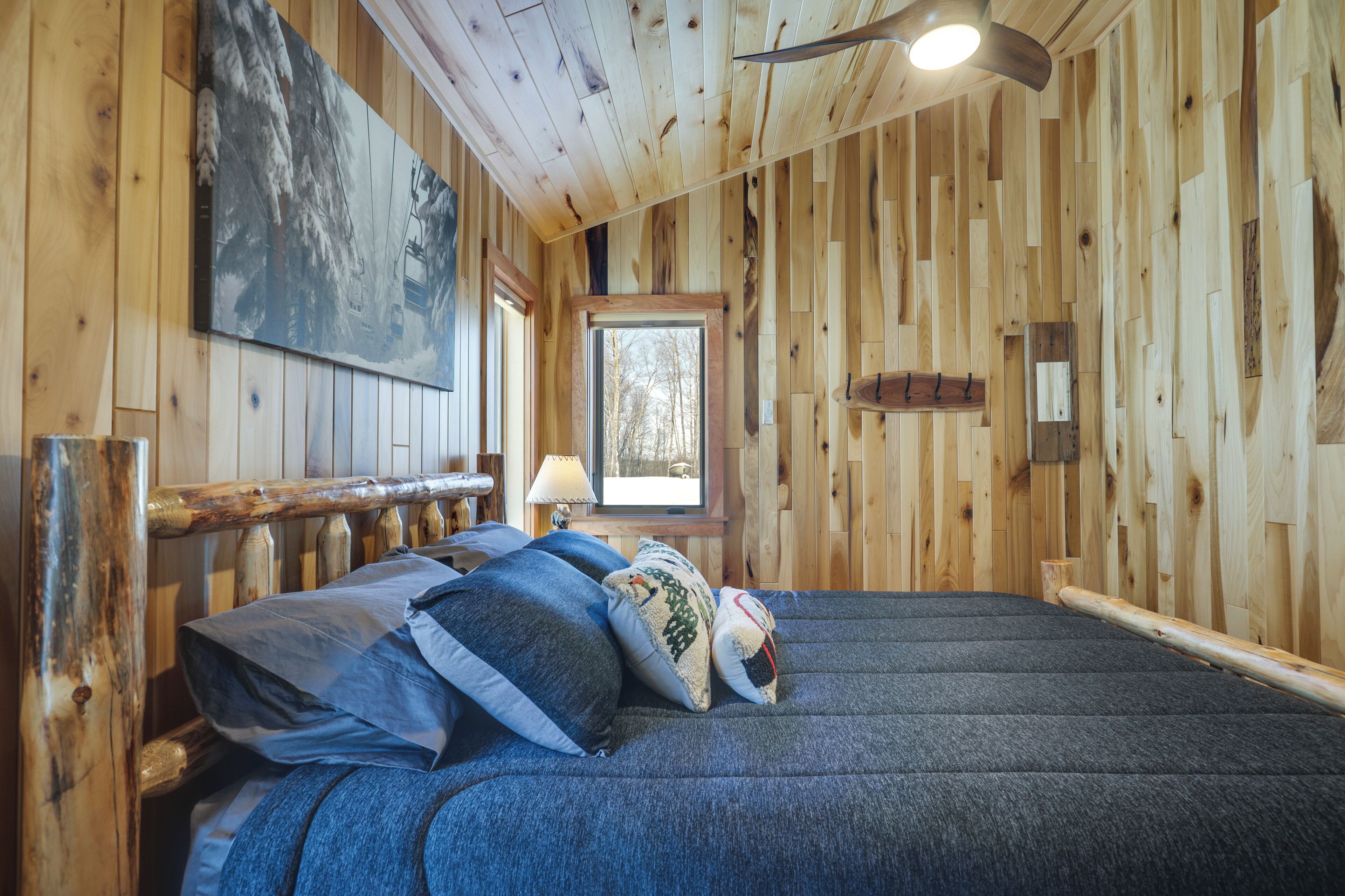 Un interior de madera con una cama, almohadas, una lámpara y una ventana.