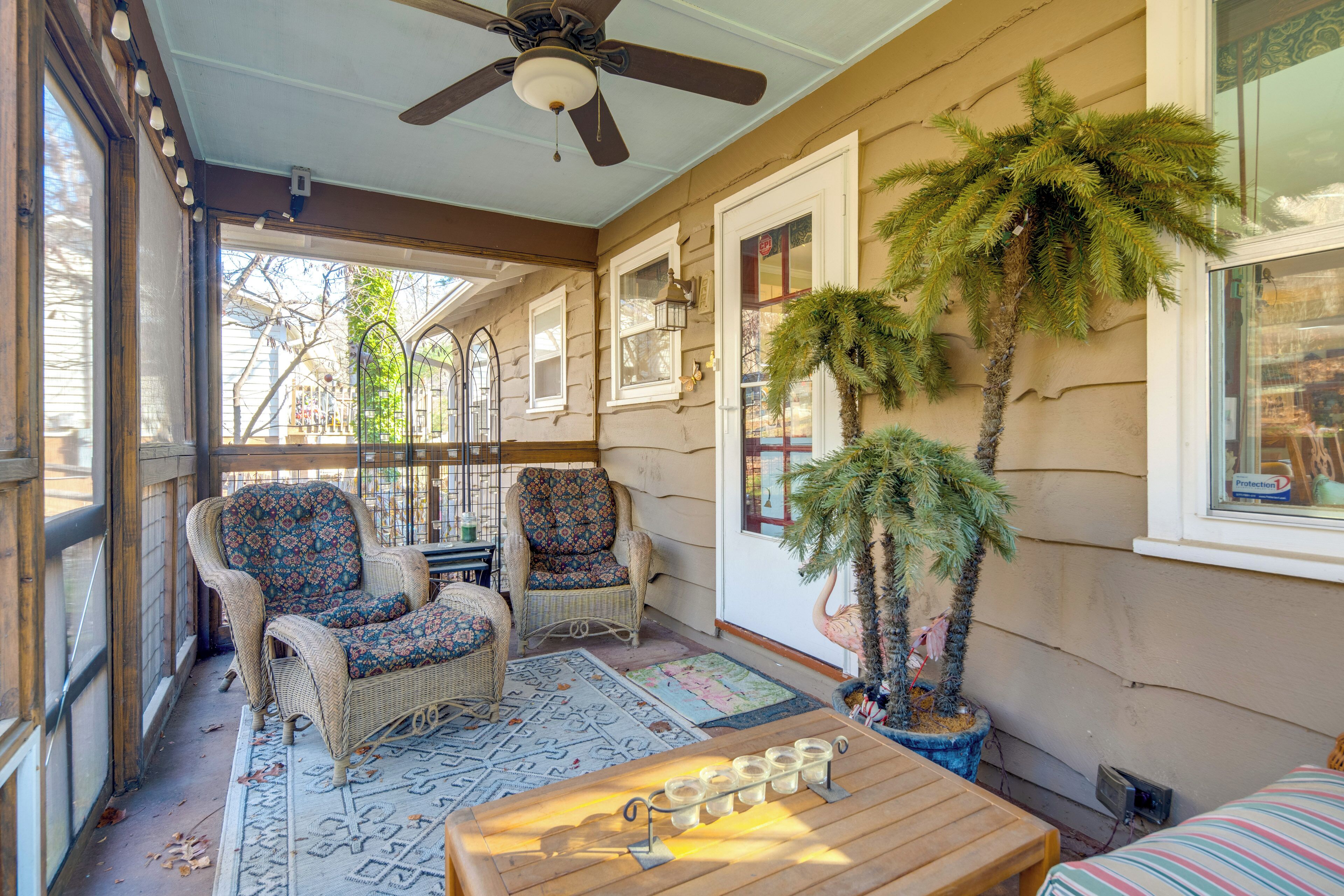 A covered porch with wicker chairs, a wooden table, and potted plants.