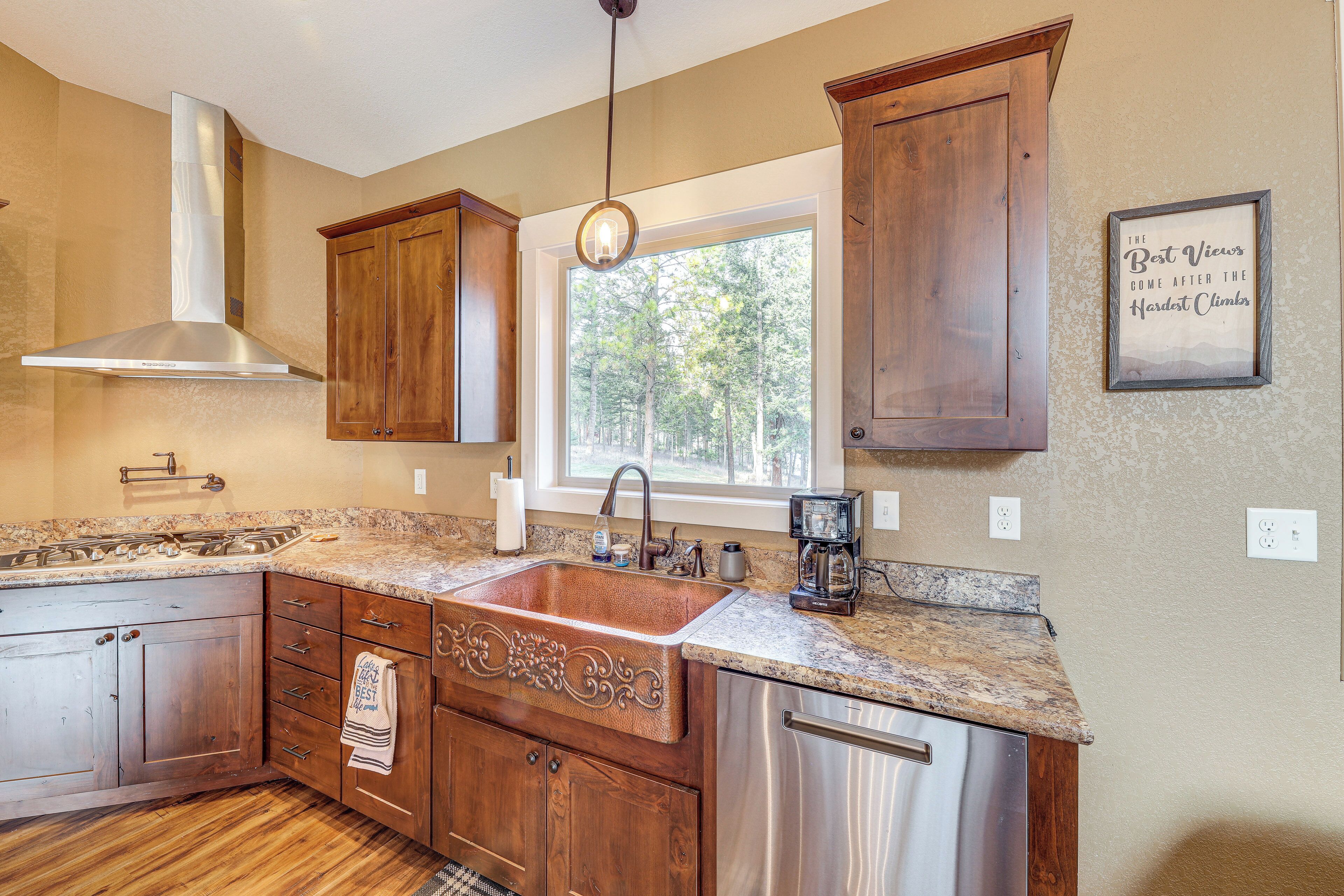 A kitchen with wooden cabinets, a stainless steel sink, and a window with a view of trees.