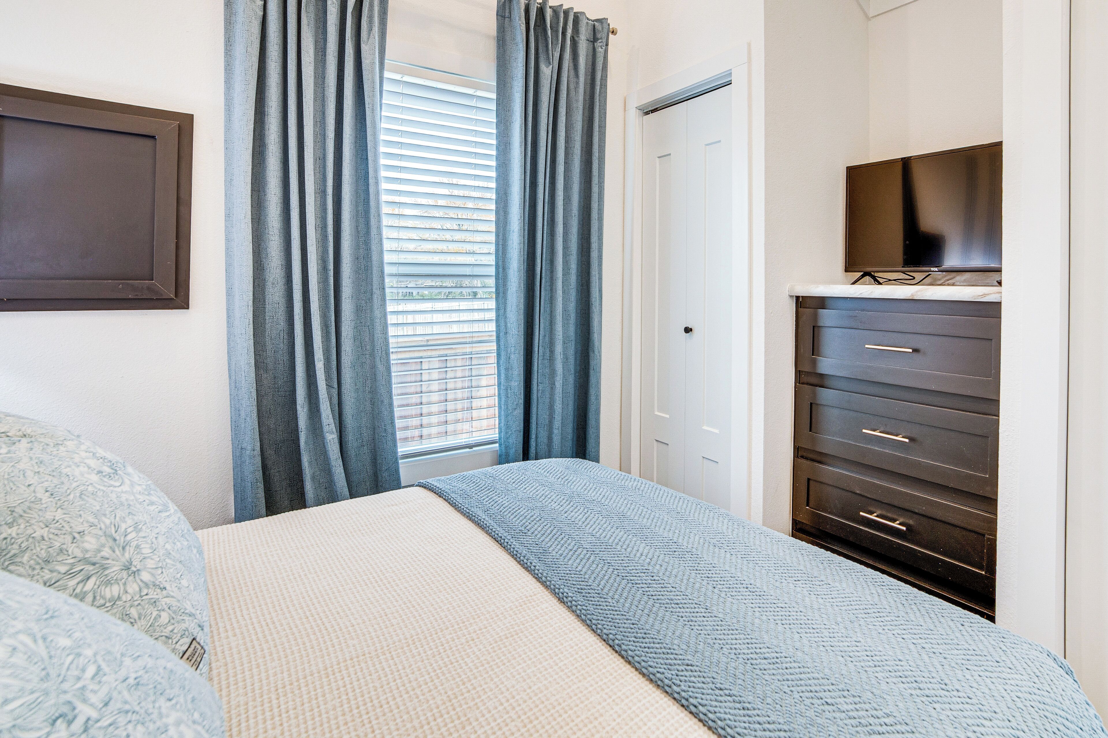 A bedroom with a bed, a dresser, a television, and a window with curtains.